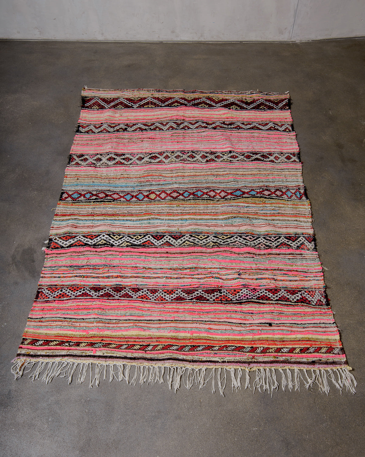Multicoloured striped rug with traditional patterns and cotton fringe on a grey floor.